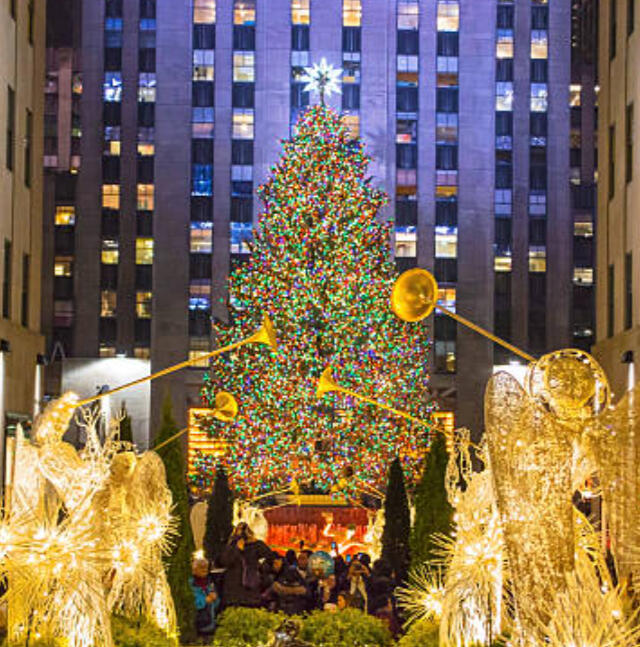 The iconic Rockefeller Center Christmas Tree lit up at night with holiday crowds in Midtown Manhattan.